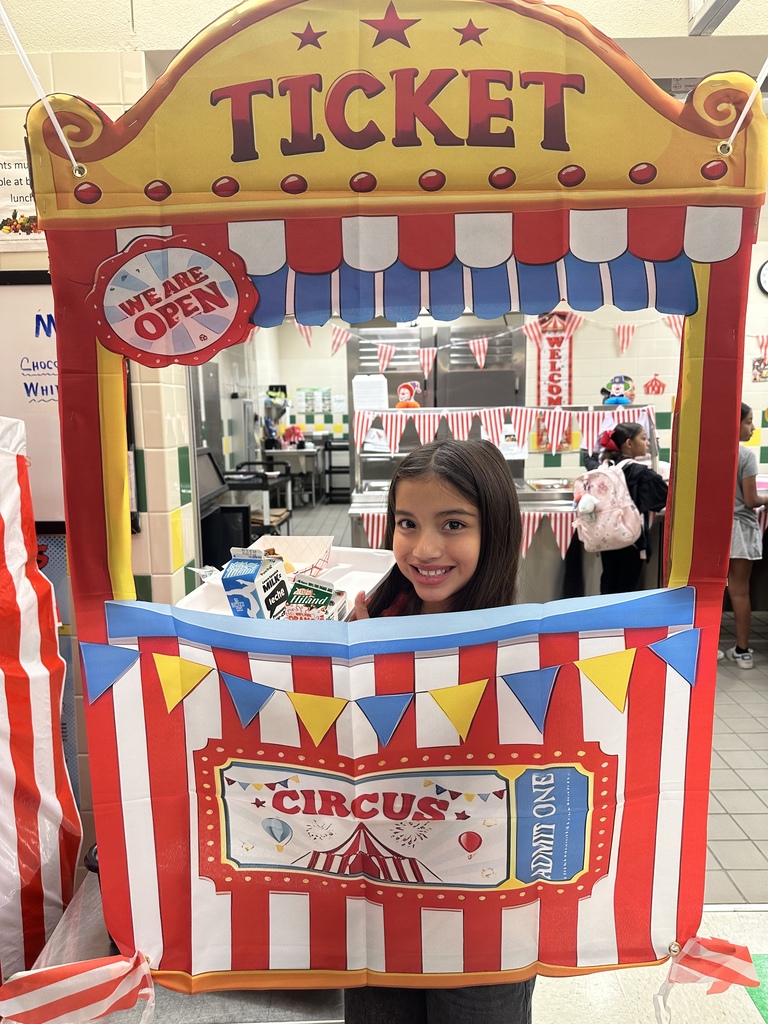 A child stands inside a ticket booth that says "Circus" on the front. The booth has red and white striped curtains.