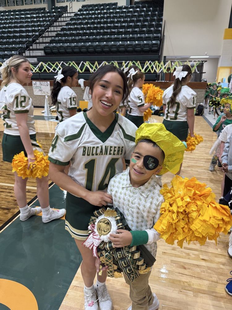 Woman and child stand together holding trophies. Child wears eye patch and yellow pom-poms. Three cheerleaders in background.