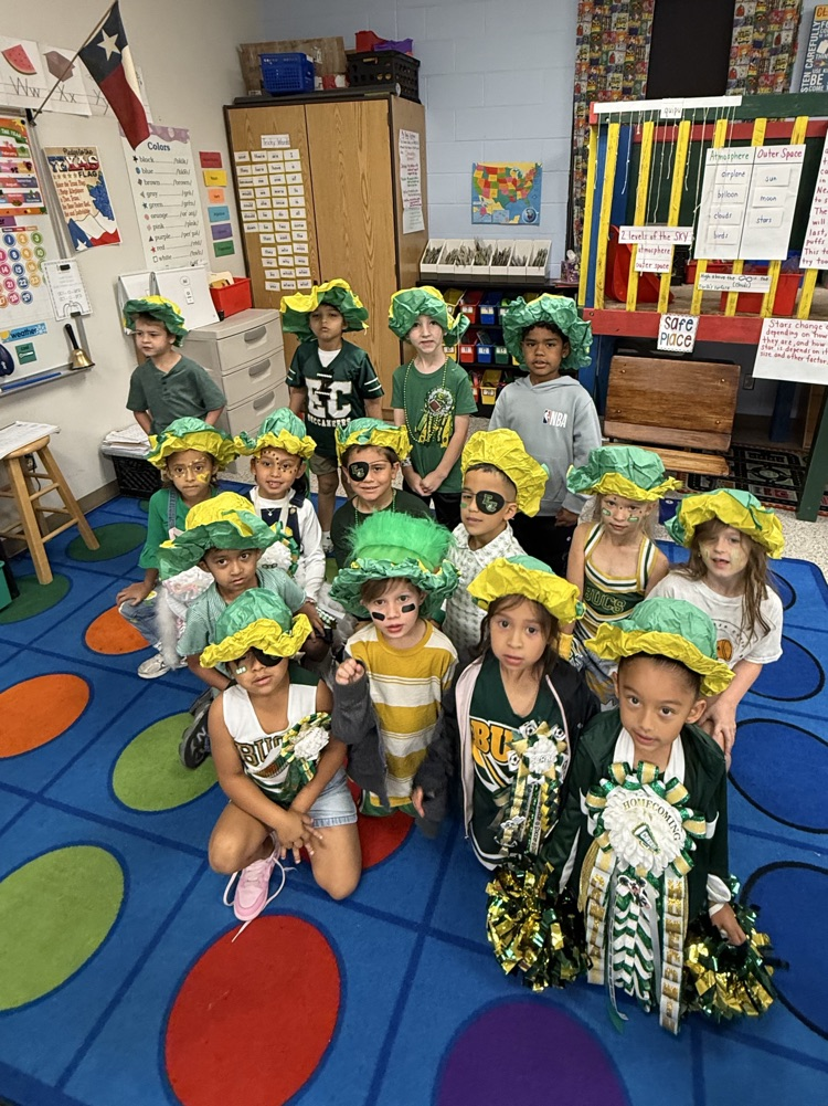 A classroom filled with children in green and yellow hats, masks, and costumes. A flag on the wall.