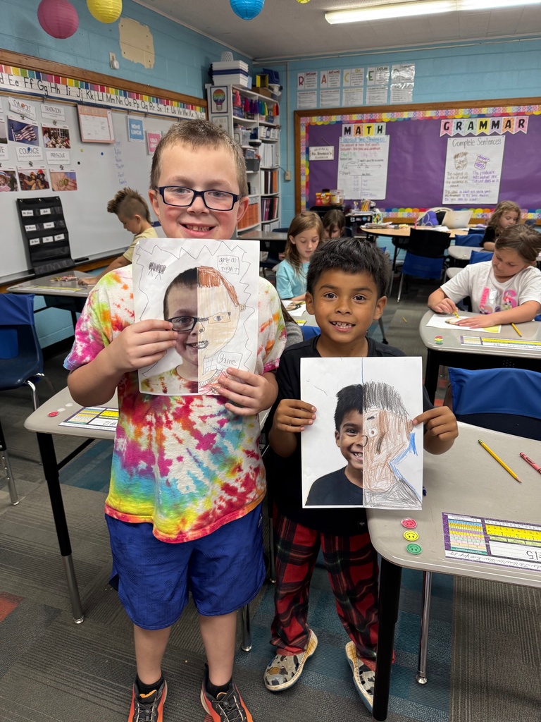 Two younger students showing off their self portraits
