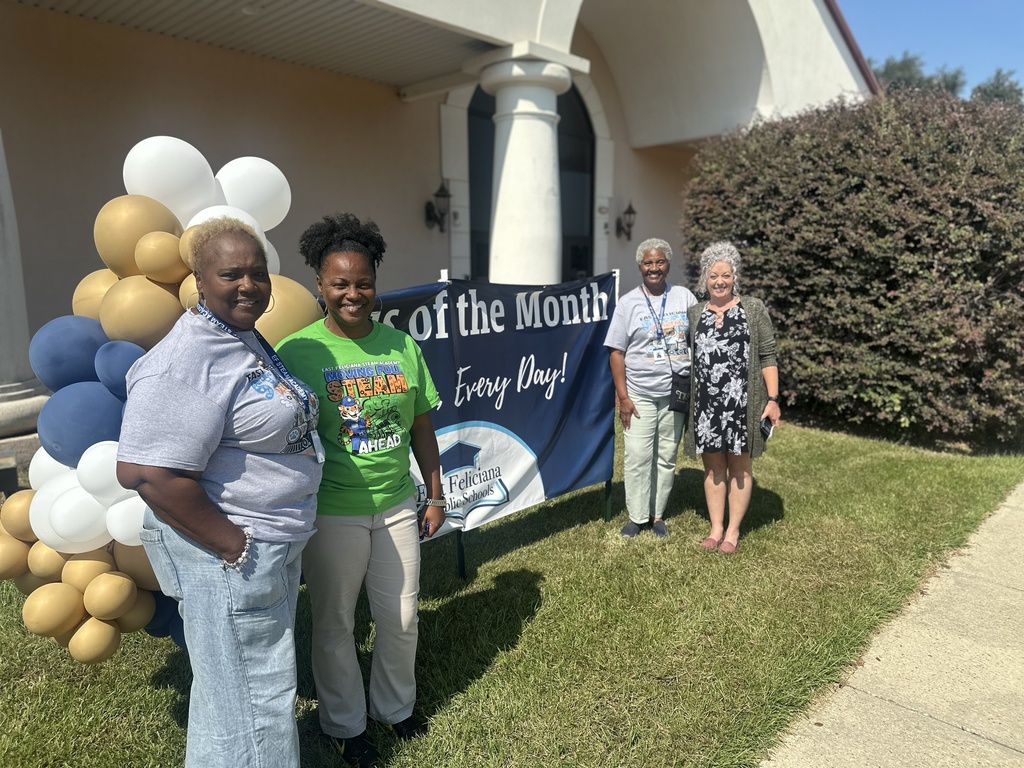 Volunteers and teachers in front of campus of the month sign.