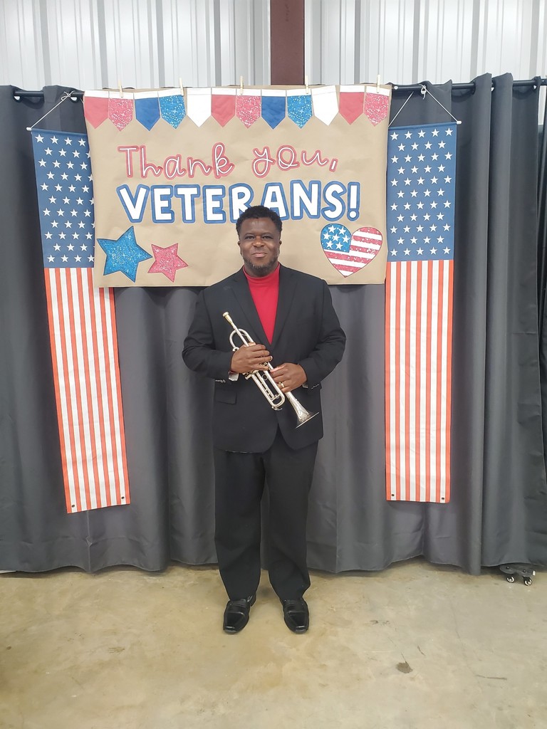 A man holding a trumpet in front of a thank you veterans sign.