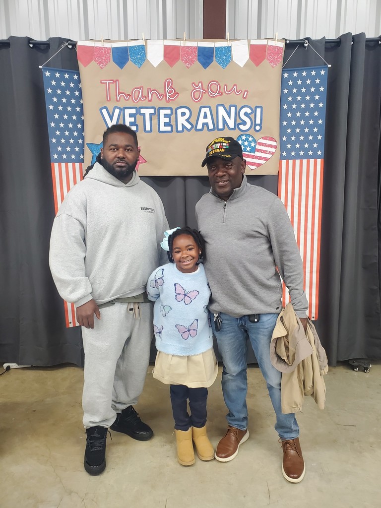 A smiling child with two adults, one in a veteran cap.