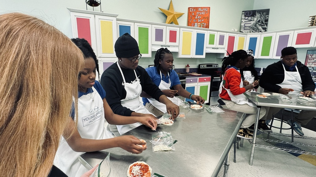 Students sit at an industrial table preparing ingredients.