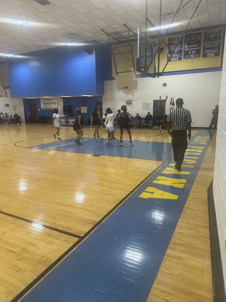 Girls basketball teams playing in a blue and gold gym with banners.