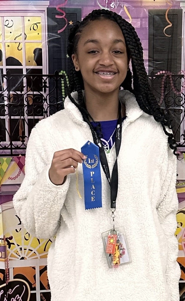 A student holds a ribbon in front of a Mardi Gras backdrop.