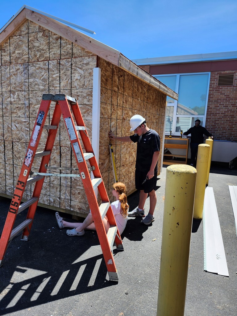 students measure and look at wood shed structure before putting siding on it