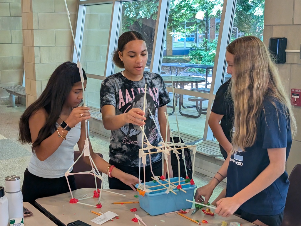 Three female students work on building a tower made of straws and tape