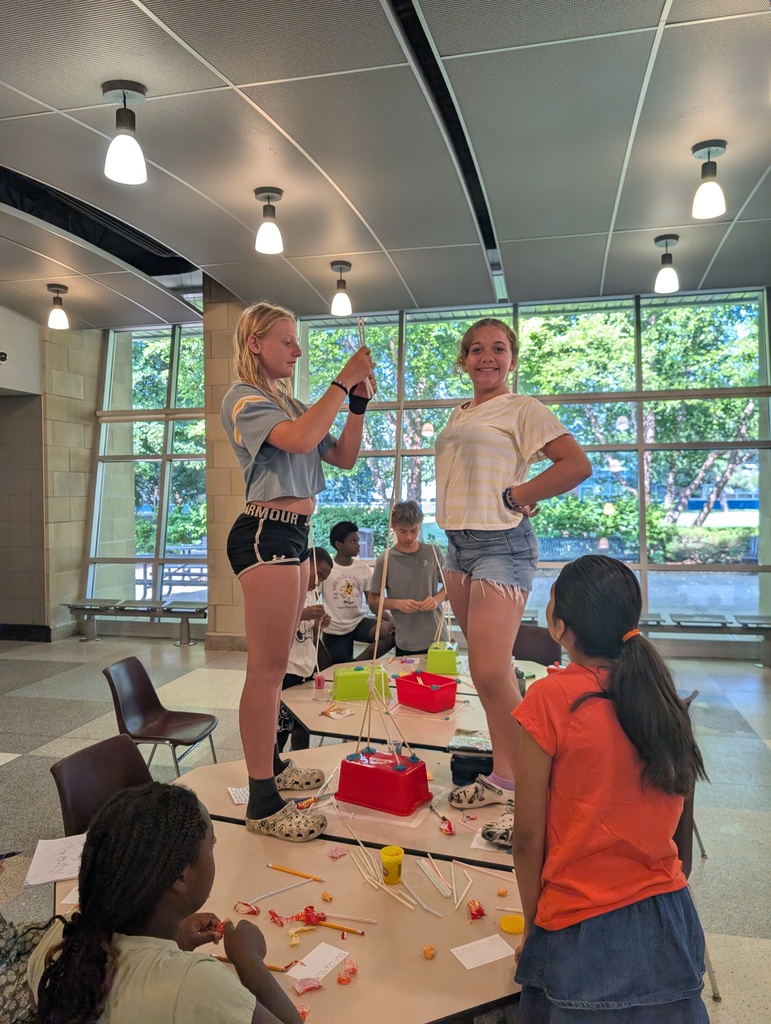 Two students smile on the table as they continue building their creation
