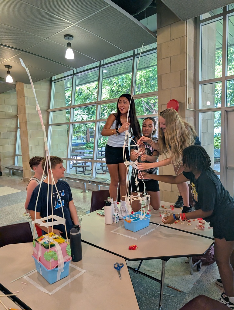Students stand on the table to work on their tower