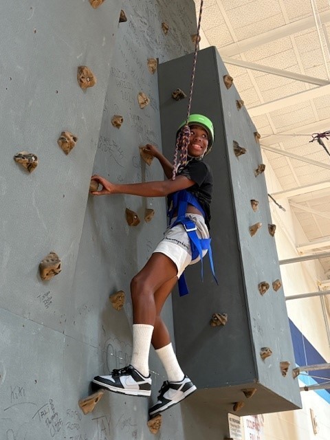 Student turns back and smiles while on the rock wall