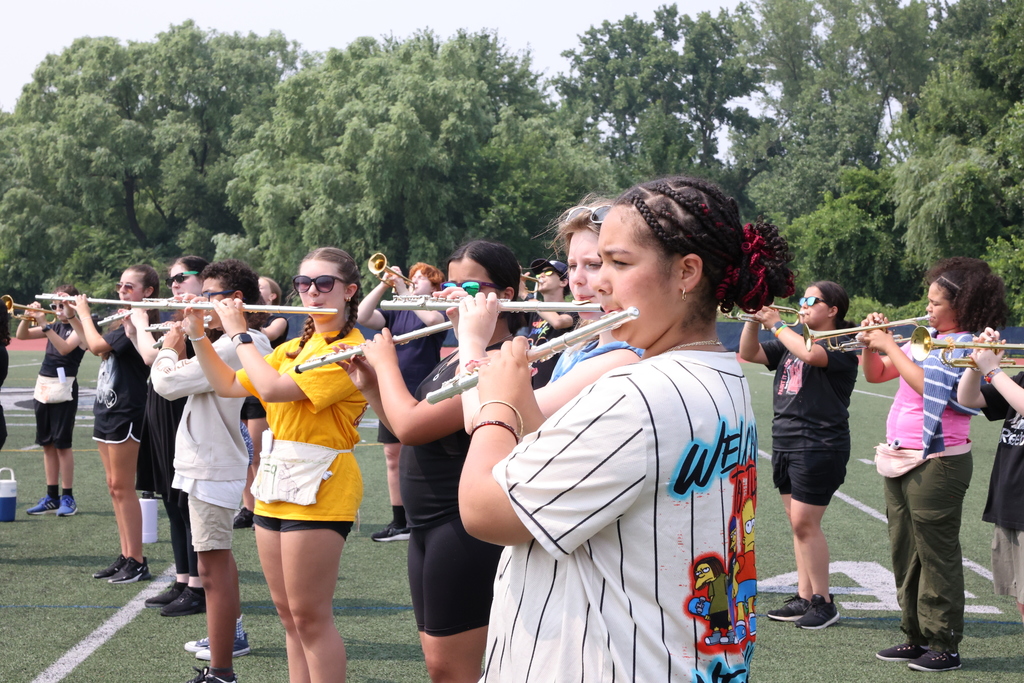 Wind section performs during the lancer band camp. students play the flute, trumpet and other instruments outside on the football field