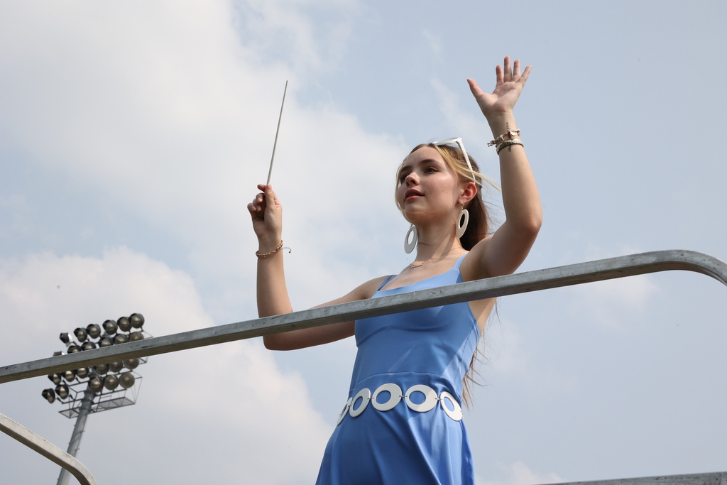 Student conducts the lancer band on a riser with her arms up