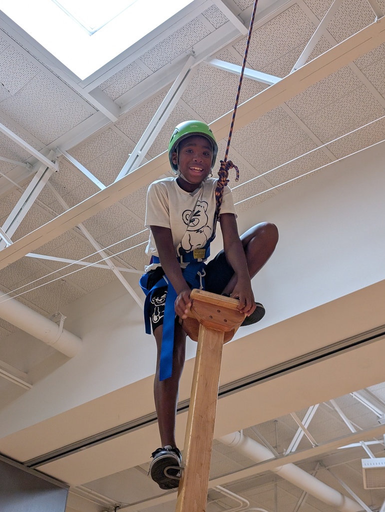 Student smiles on a wood structure with rope tied around and a helmet
