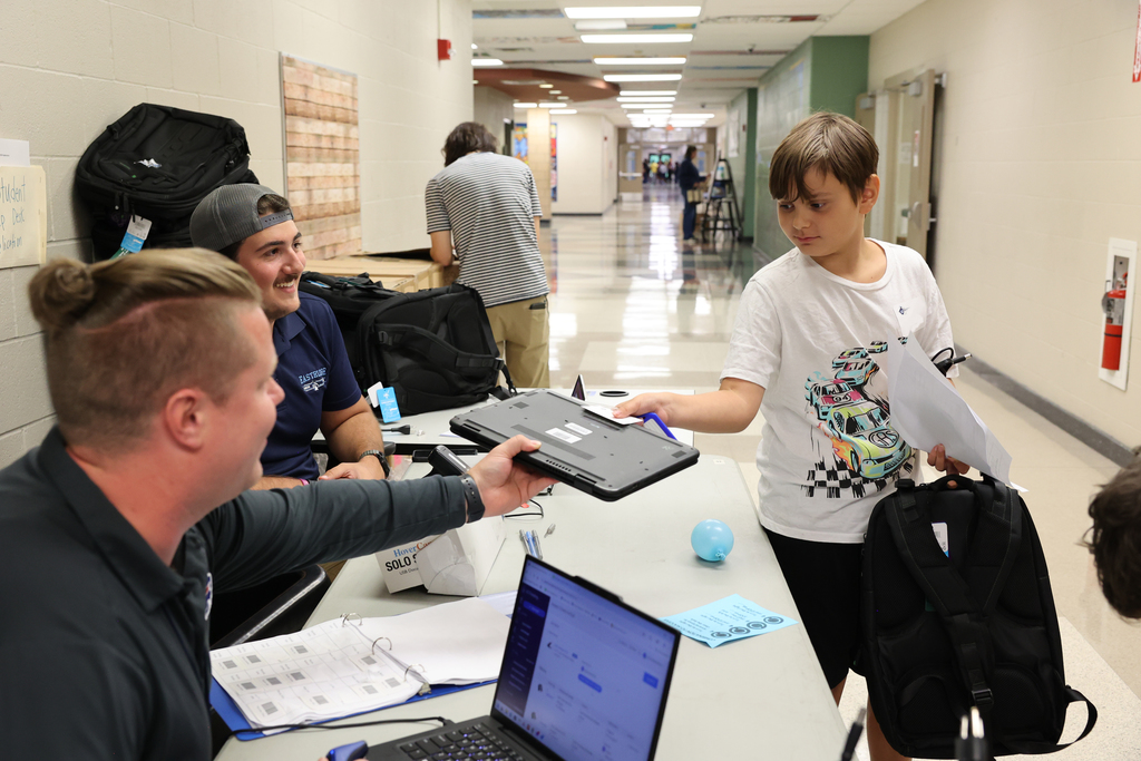 IT employees hand laptop to an EIMS student