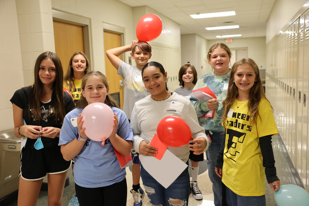 Students smile with balloons in the middle school hallway