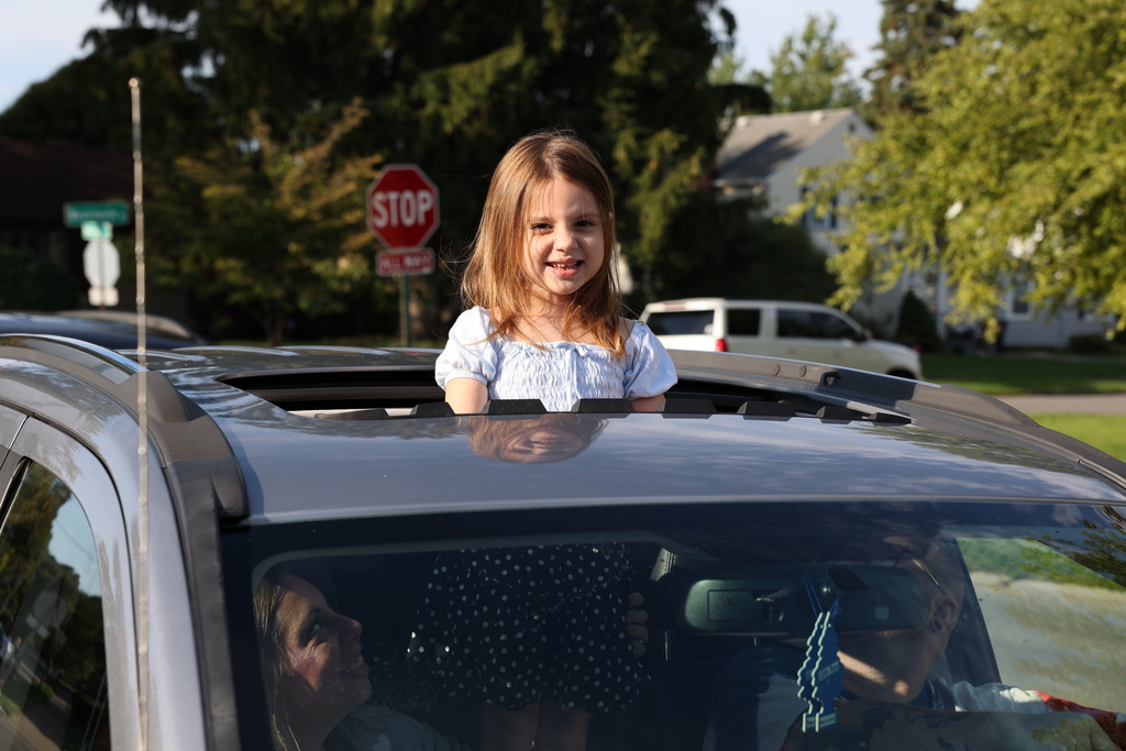 Student stands out of the sunroof while waiting in the car line