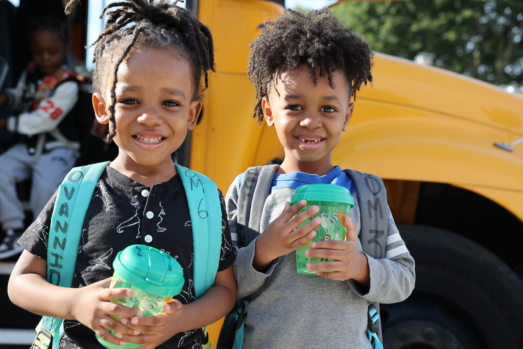 Two kids smile outside of the school bus with their water cups