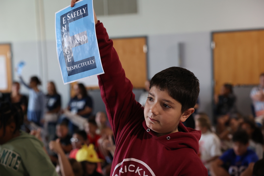 Student holds up E sign and stands up during an assembly