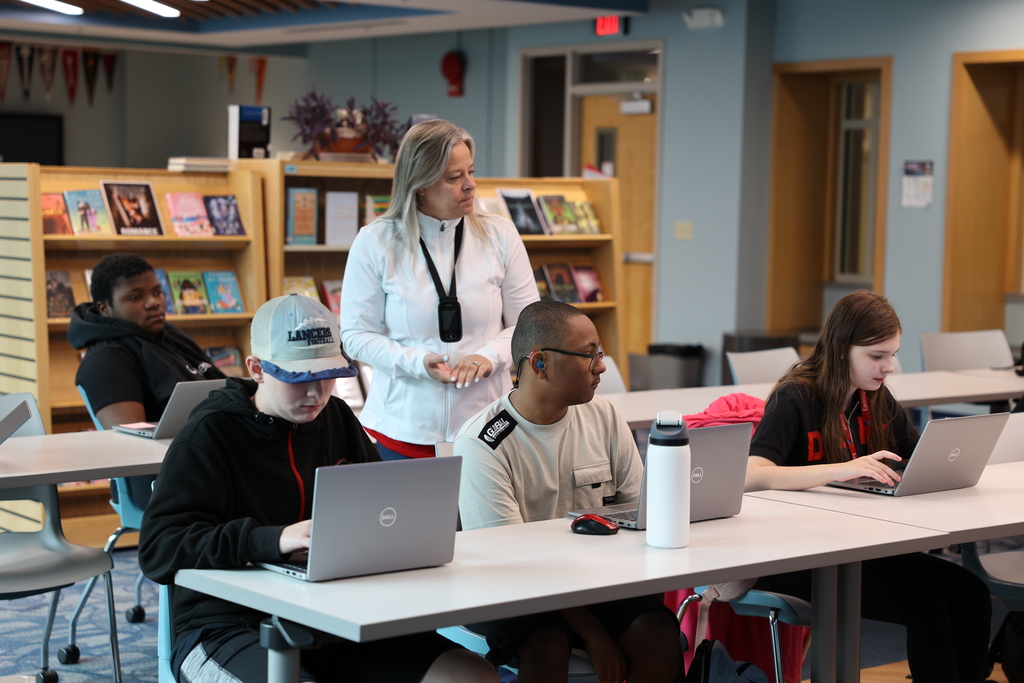 Students practice using the library database with their laptops and with the librarian overlooking