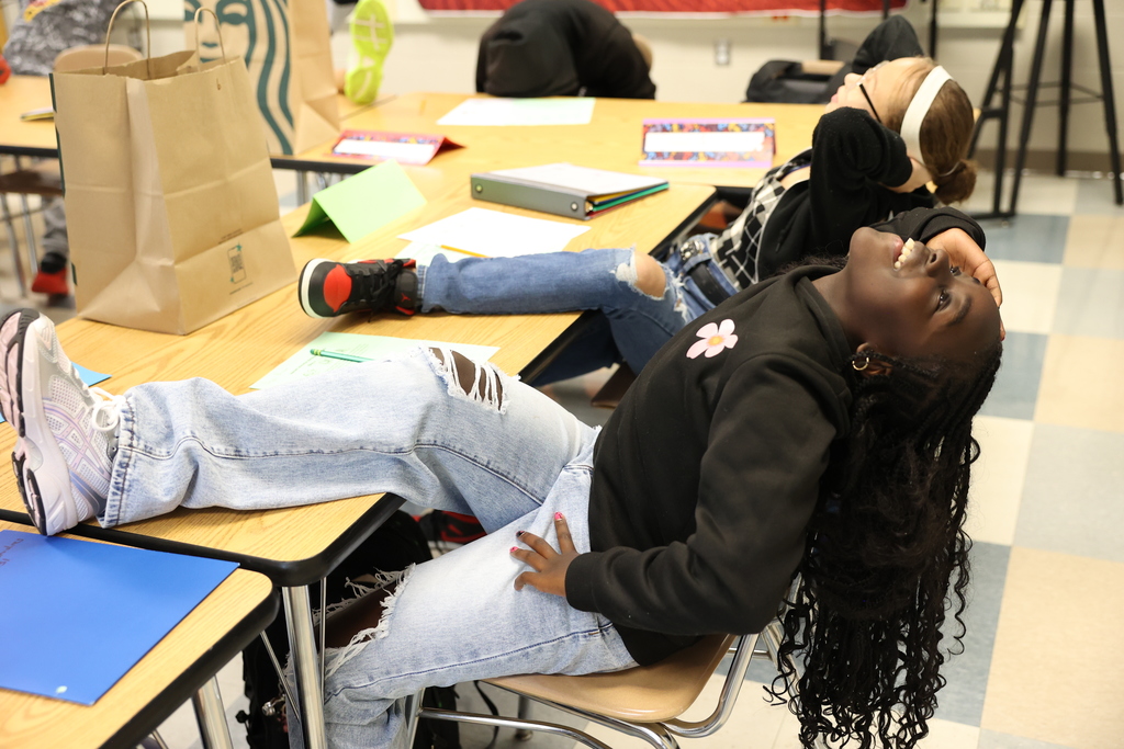 Student participates in history lesson and leans back with foot on desk listening to teacher's directions