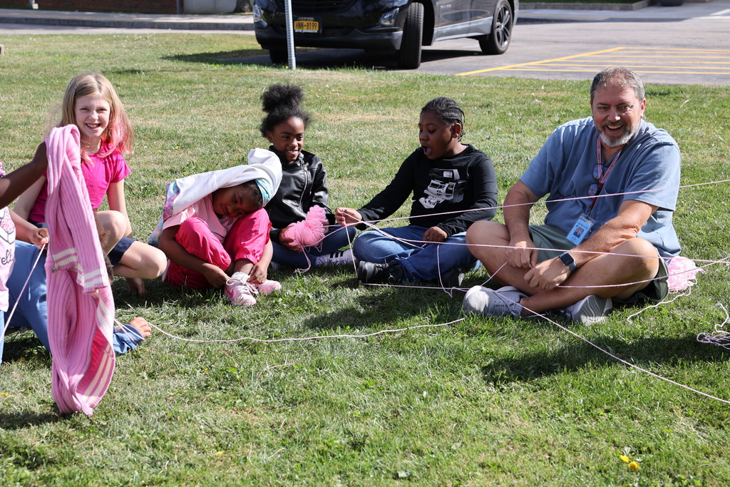 Students laugh with teacher as they toss the yarn around