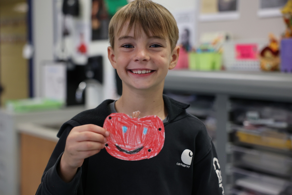 student holds up art and smiles