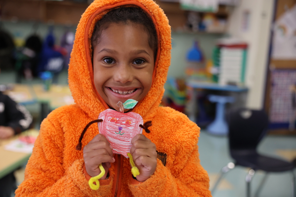 student holds up art and smiles