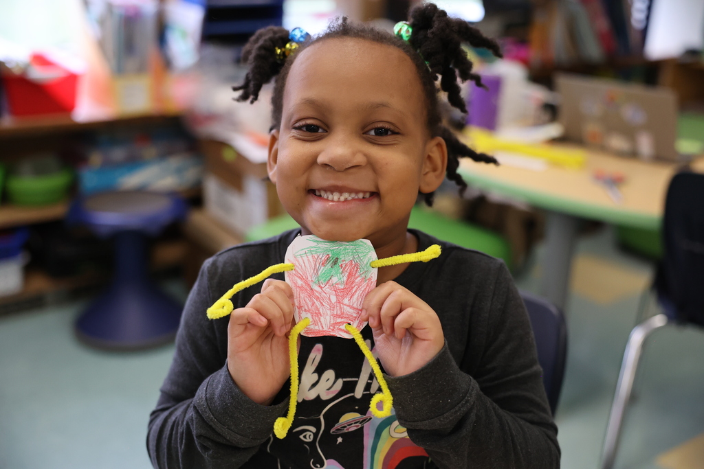 student holds up art and smiles