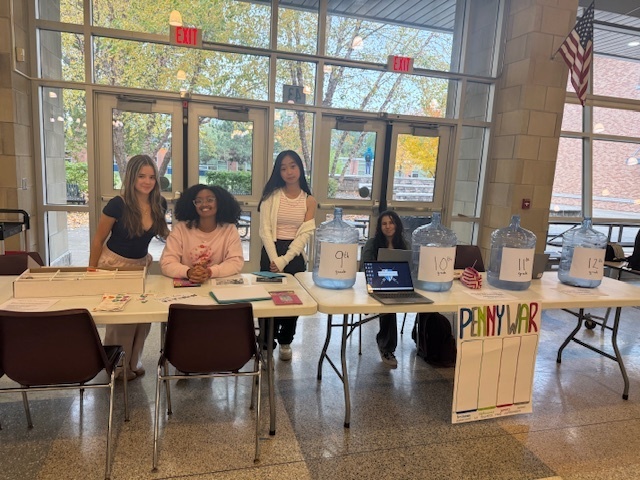 Students sit behind tables with collection jars for coins