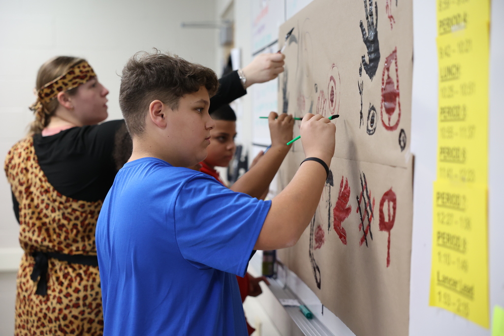 students paint on large paper on the wall