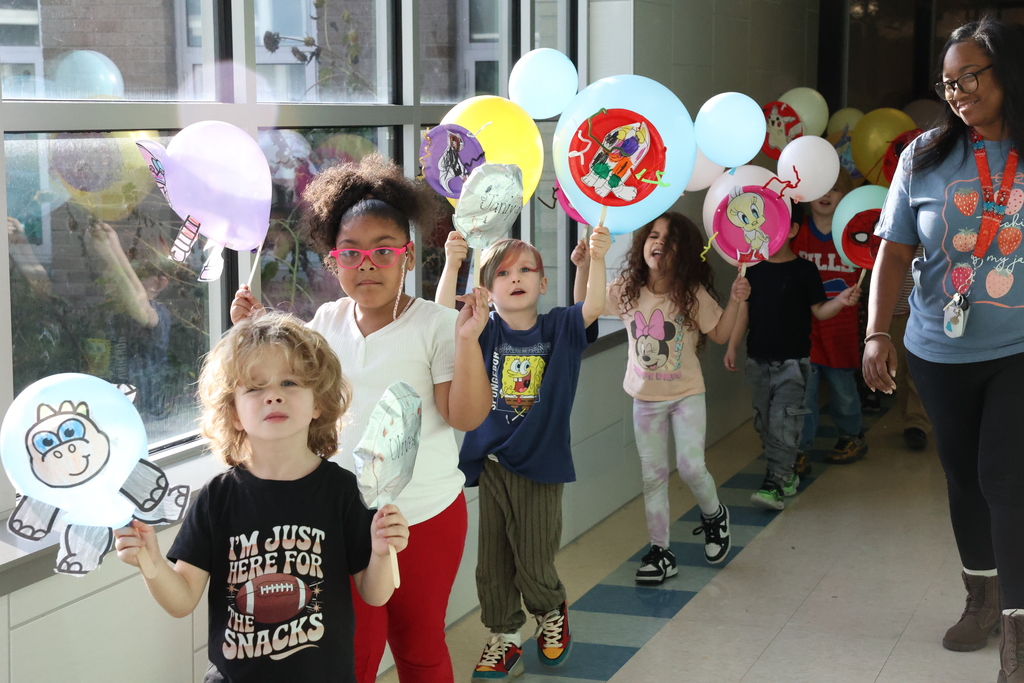 Kids hold up balloons and walk down the hall