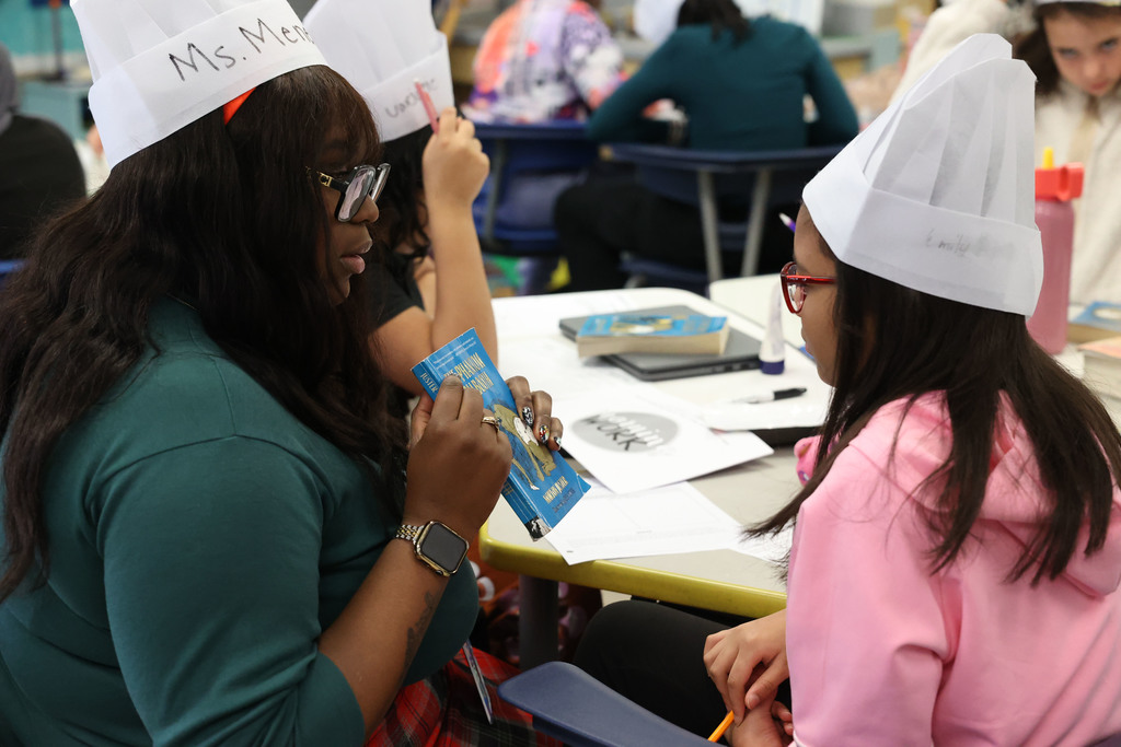 teacher holds up the Phantom Tollbooth and helps student with worksheet