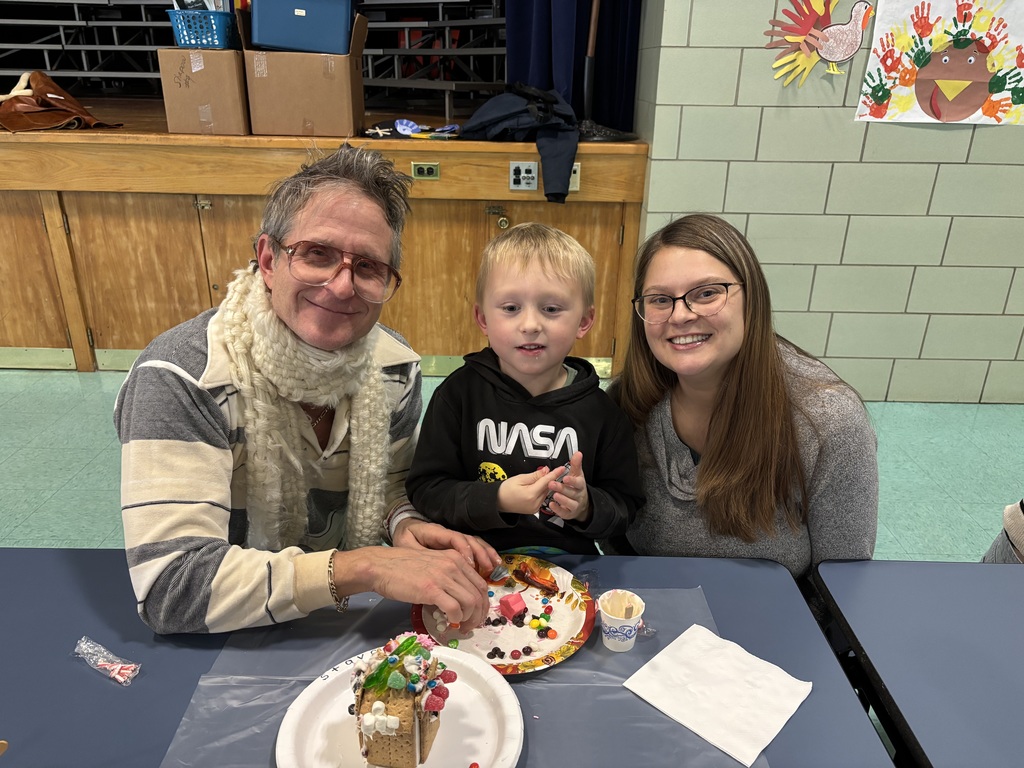 Student and famiy pose for a photo while creating gingerbread houses