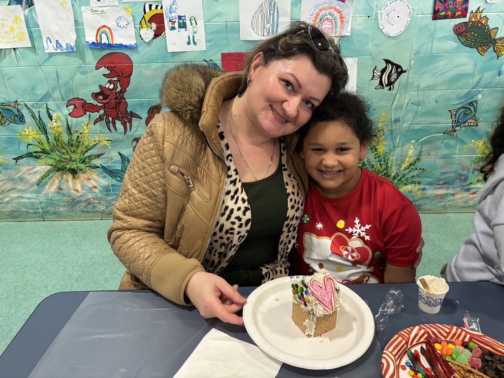 parent and student pose for a photo with completed gingerbread house
