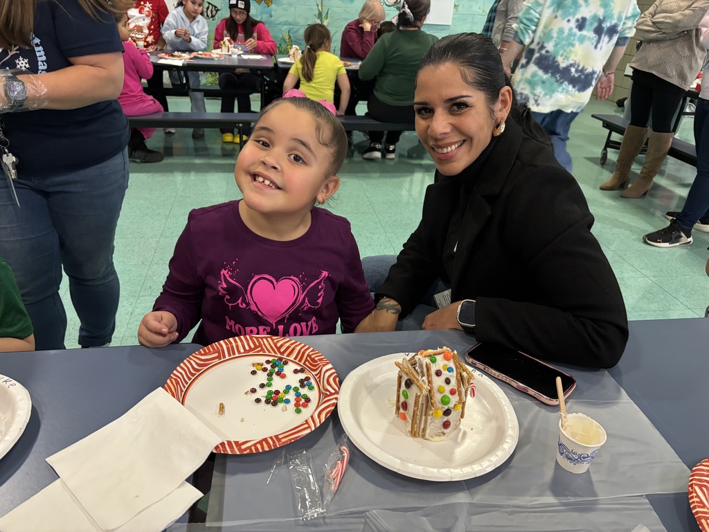 Student and parent pose for a photo while making gingerbread houses