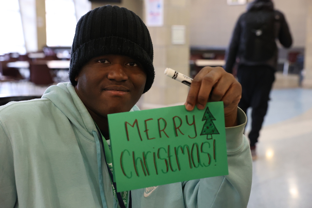 student holds up merry christmas card
