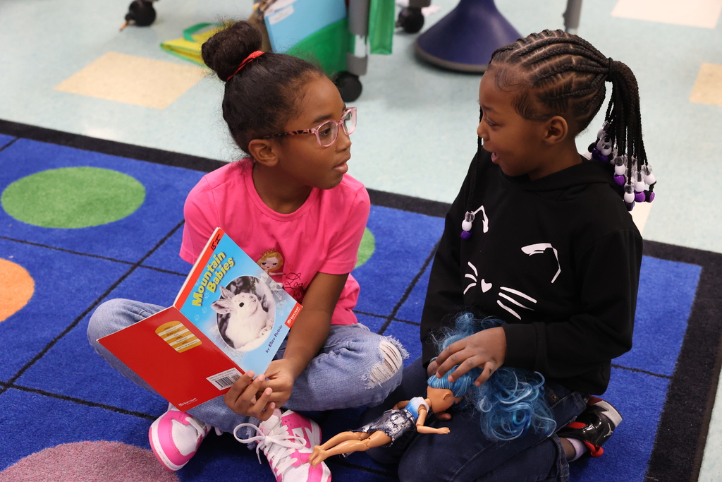 students talk to one another while holidng a book and a doll
