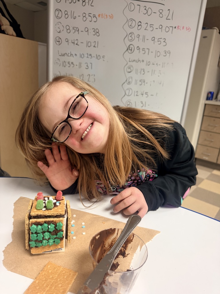 Student waves while making gingerbread house