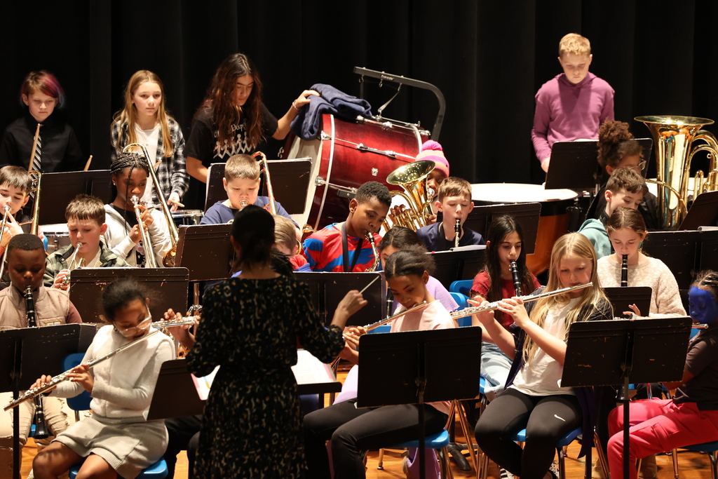 Student play instruments with composer conducting them