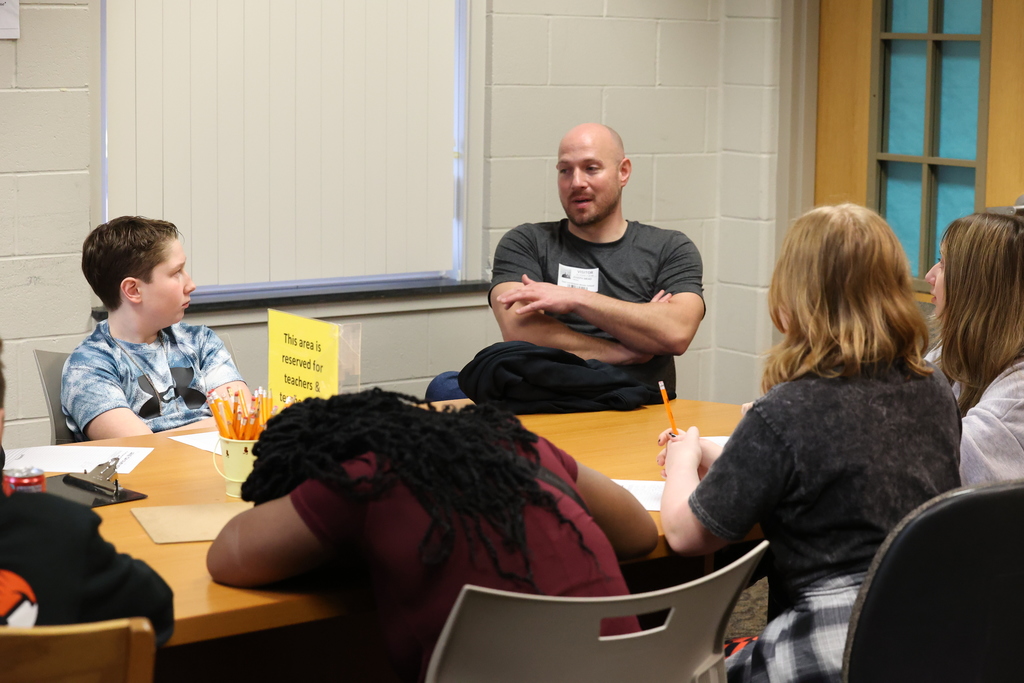 Students listen to guest speaker at a table