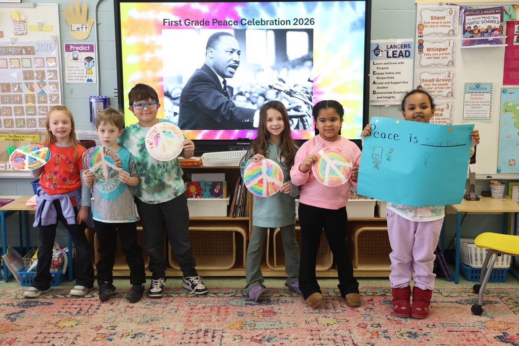 Students hold up peace signs in front of First Grade Peace Celebration 2026