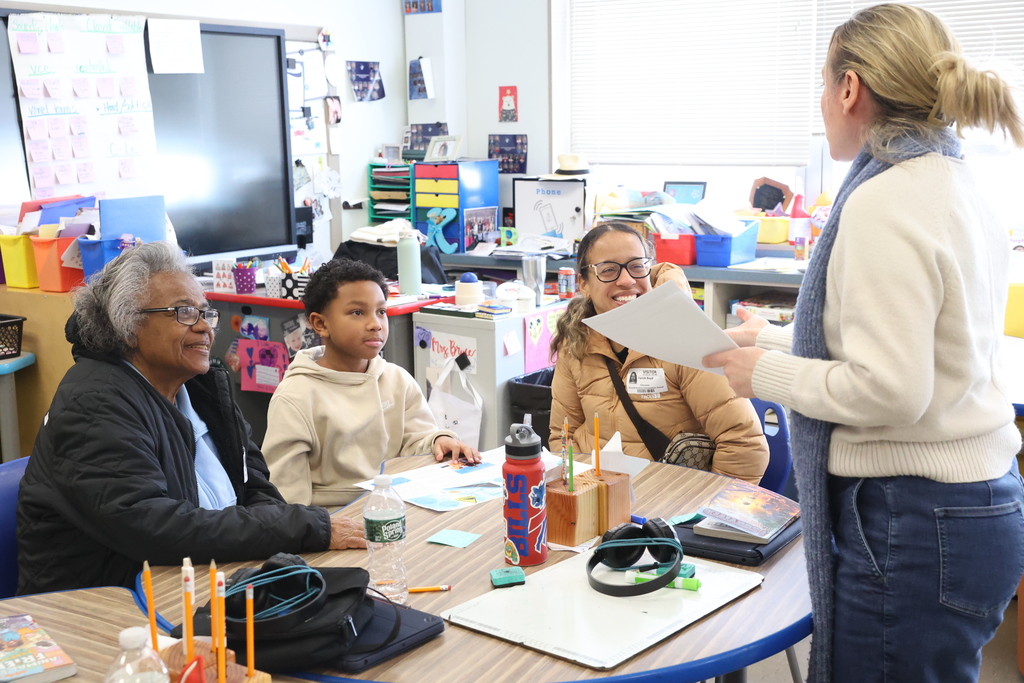Student listens to teacher with family members and smiles