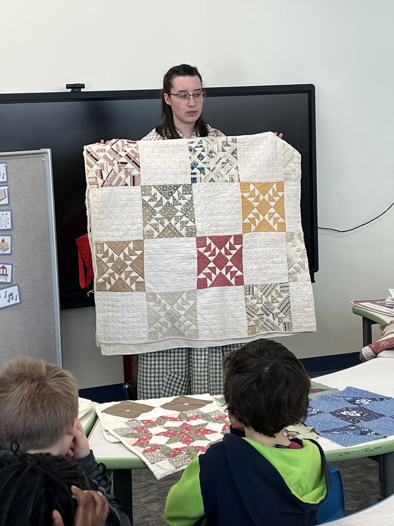 visitor shows students a quilt