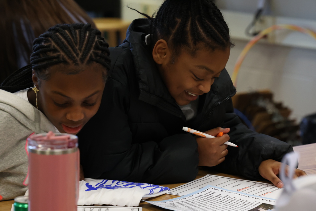 students smile and work on worksheet at desk