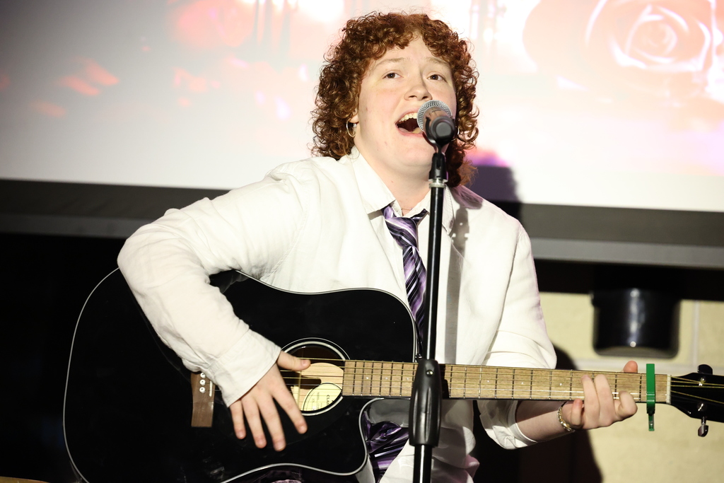 student sings into the microphone while playing guitar