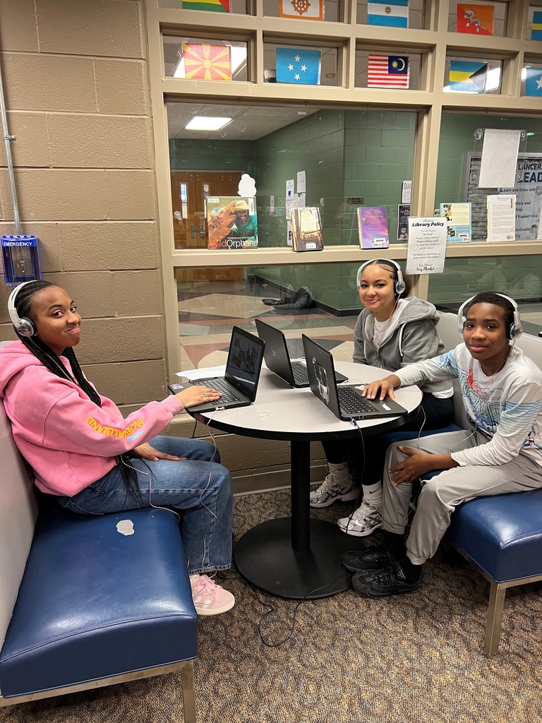 students sit in a booth in the library with their computers and headphones