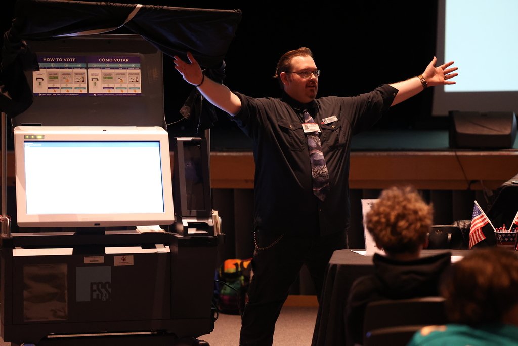 guest opens arms near voting machine
