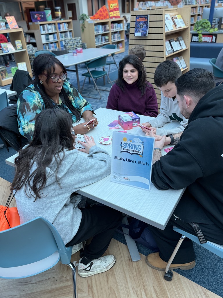 Student gather at a table and play a game called Blah, Blah, Blah for Spring into Literacy Night in the library