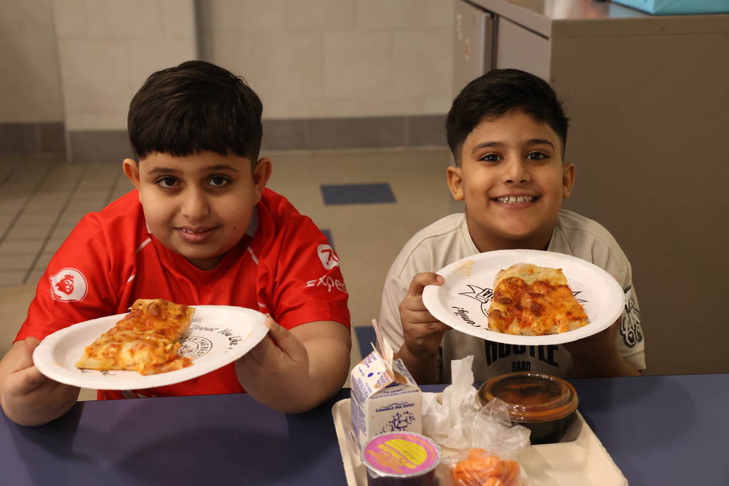 students smile while getting ready to eat their pizza treat